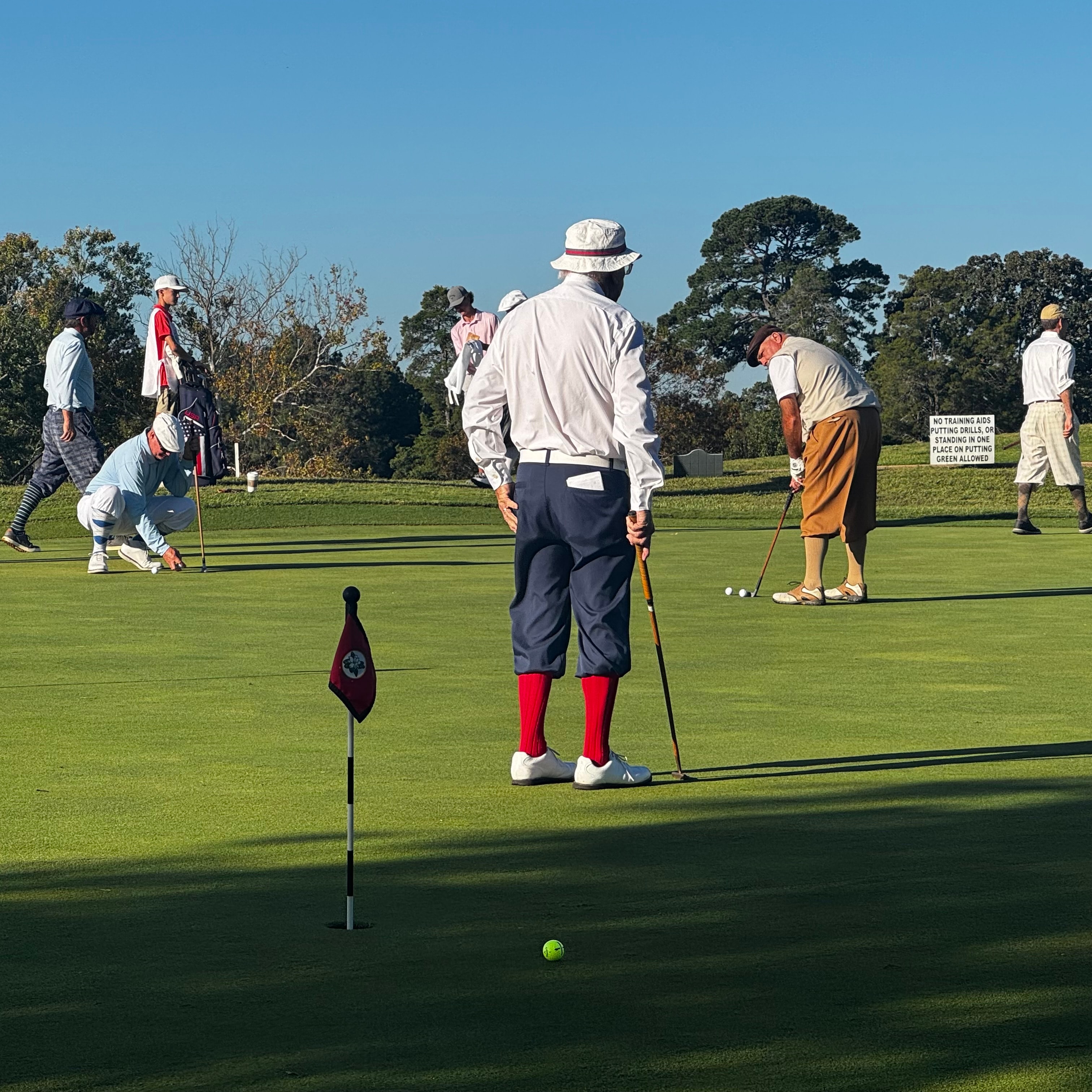 Hickory golfers in period attire putting on the green